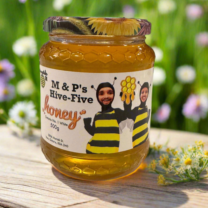 Jar of M & P's Hive-Five Honey with a bee-themed label on a wooden surface with flowers in the background